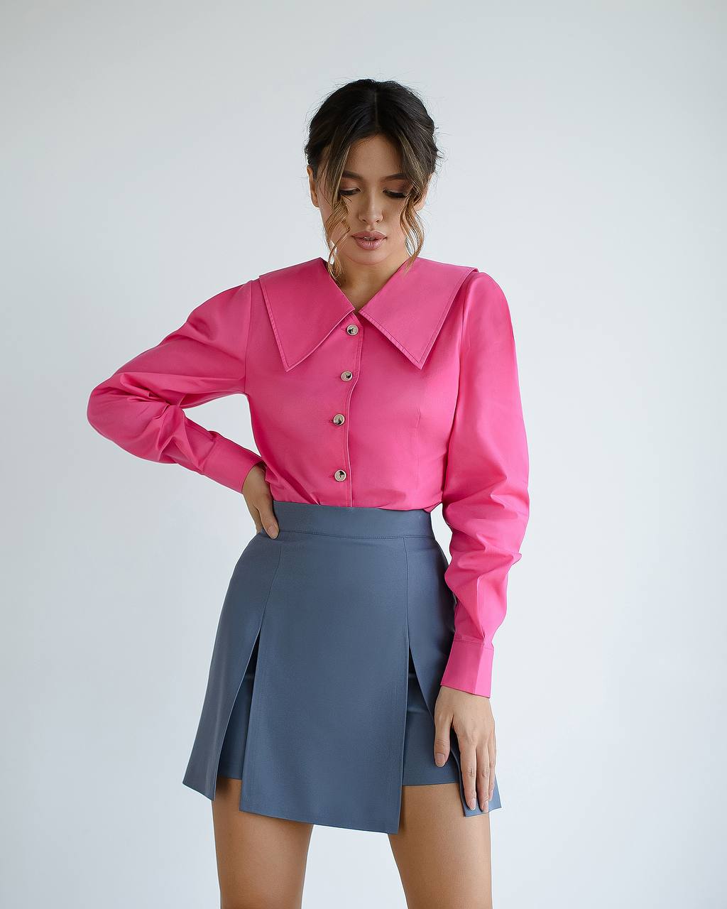 Woman wearing a pink blouse with a high collar and a gray skirt on a white background