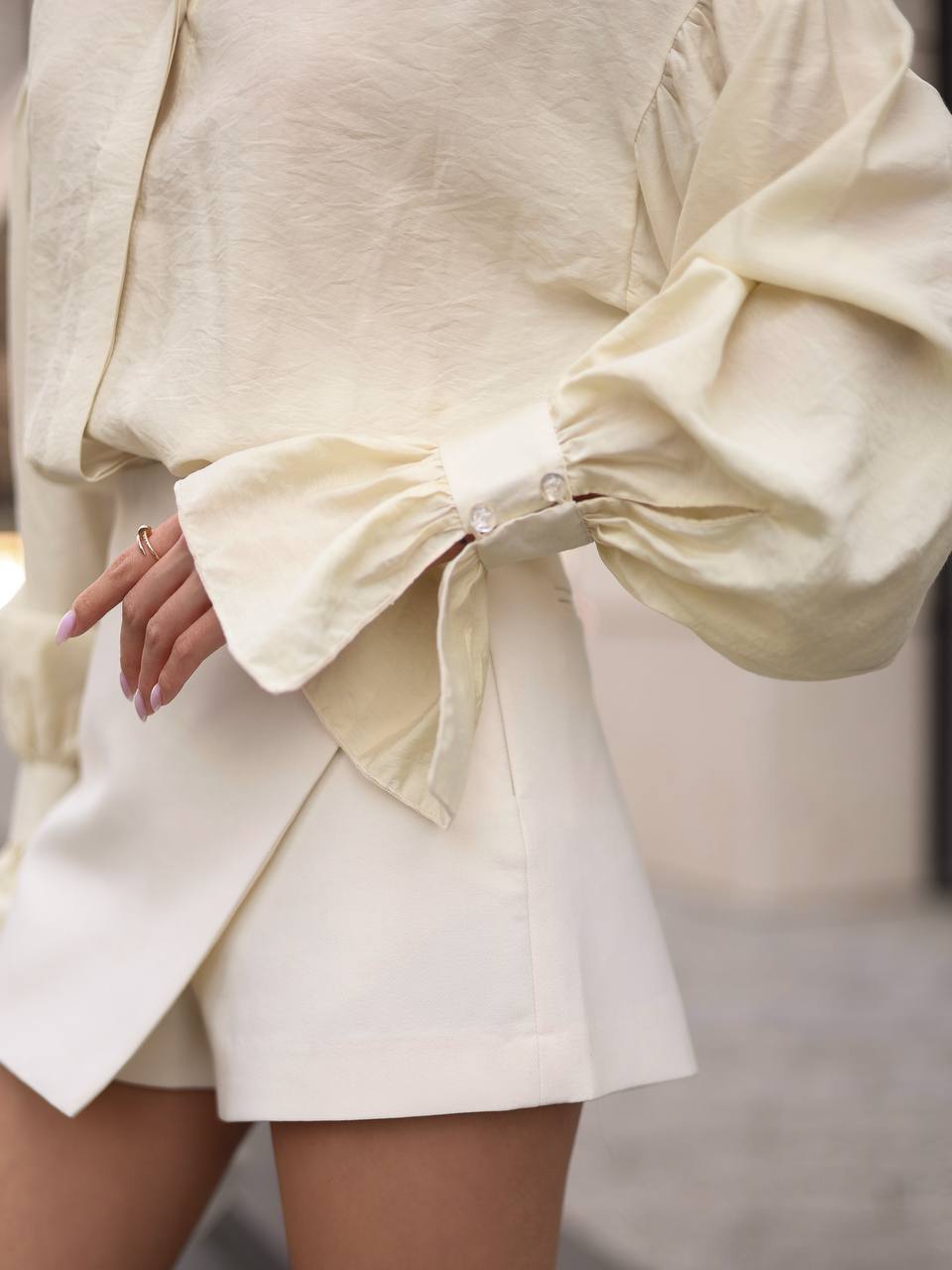 Person wearing a light-colored outfit with a bow detail on a blurred background