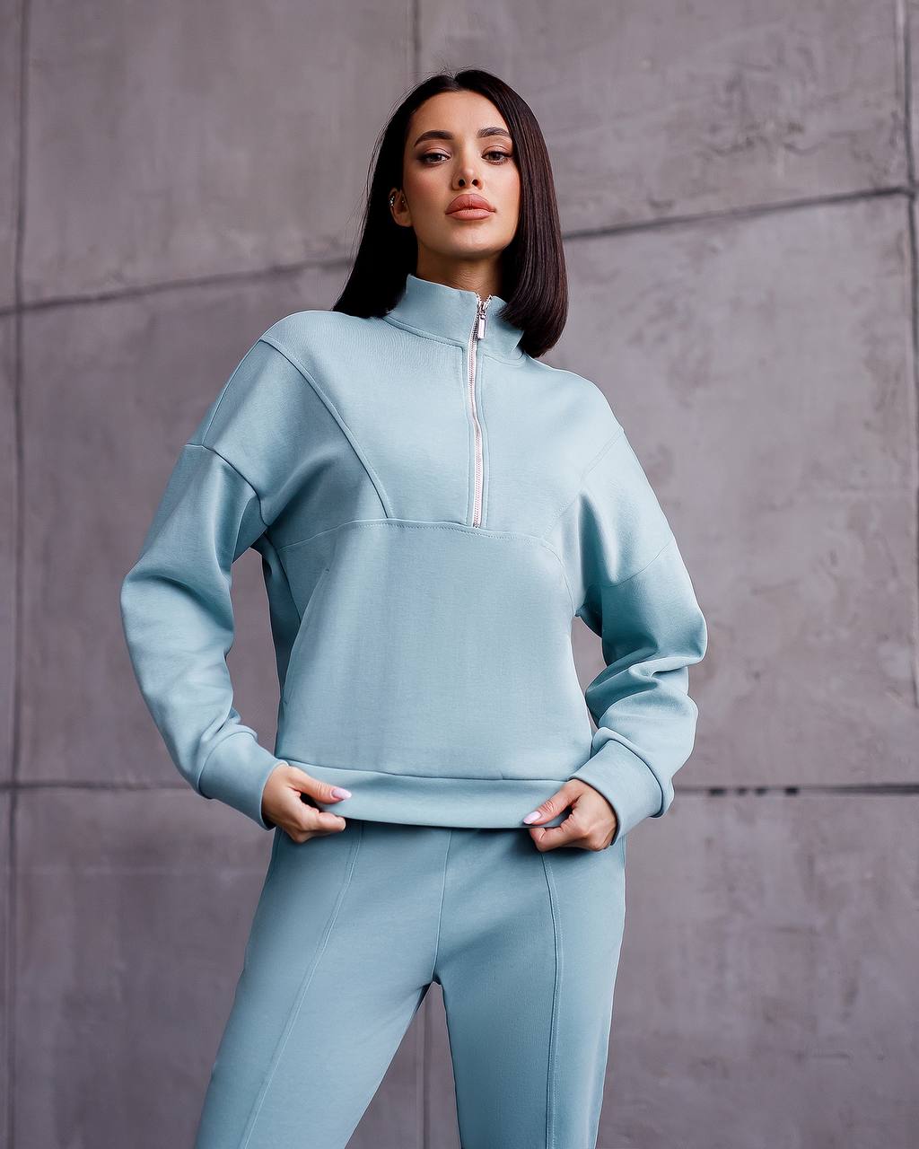 Woman wearing a light blue tracksuit against a gray background