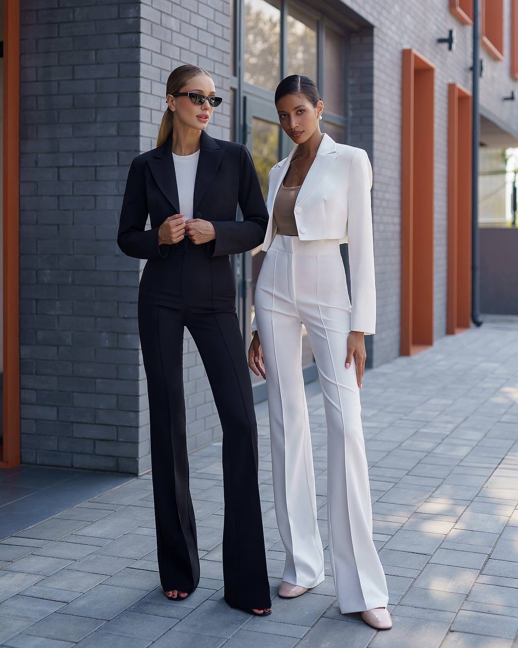 Two women in black and white suits standing on a sidewalk.