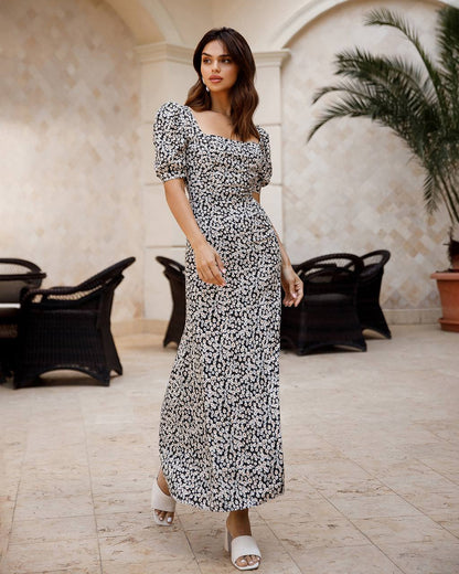 Woman in a floral dress standing in an elegant indoor setting with marble floors and decorative elements.