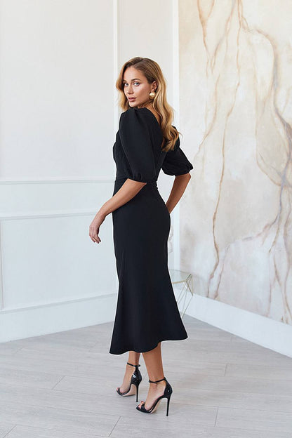 Woman wearing a black dress standing against a marble wall.