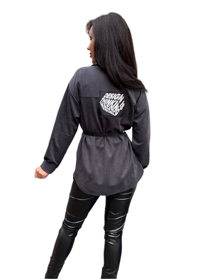 Person wearing a dark gray long-sleeve shirt with a logo on the back, standing against a white background.