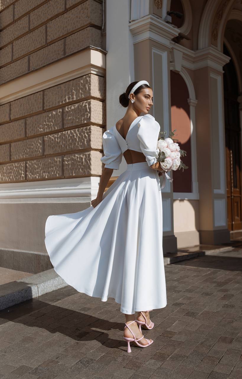 Woman in a white wedding dress standing in front of an architectural building.