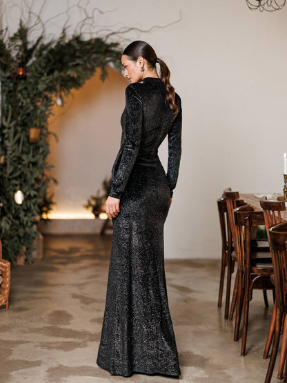 Woman in a black sequin gown standing in a decorated room with a Christmas tree and wooden furniture.