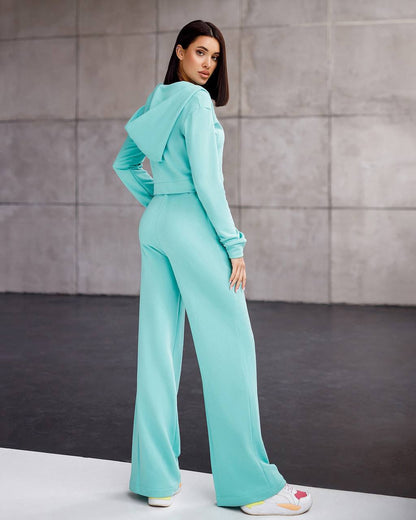 Woman wearing a turquoise outfit standing against a gray wall.