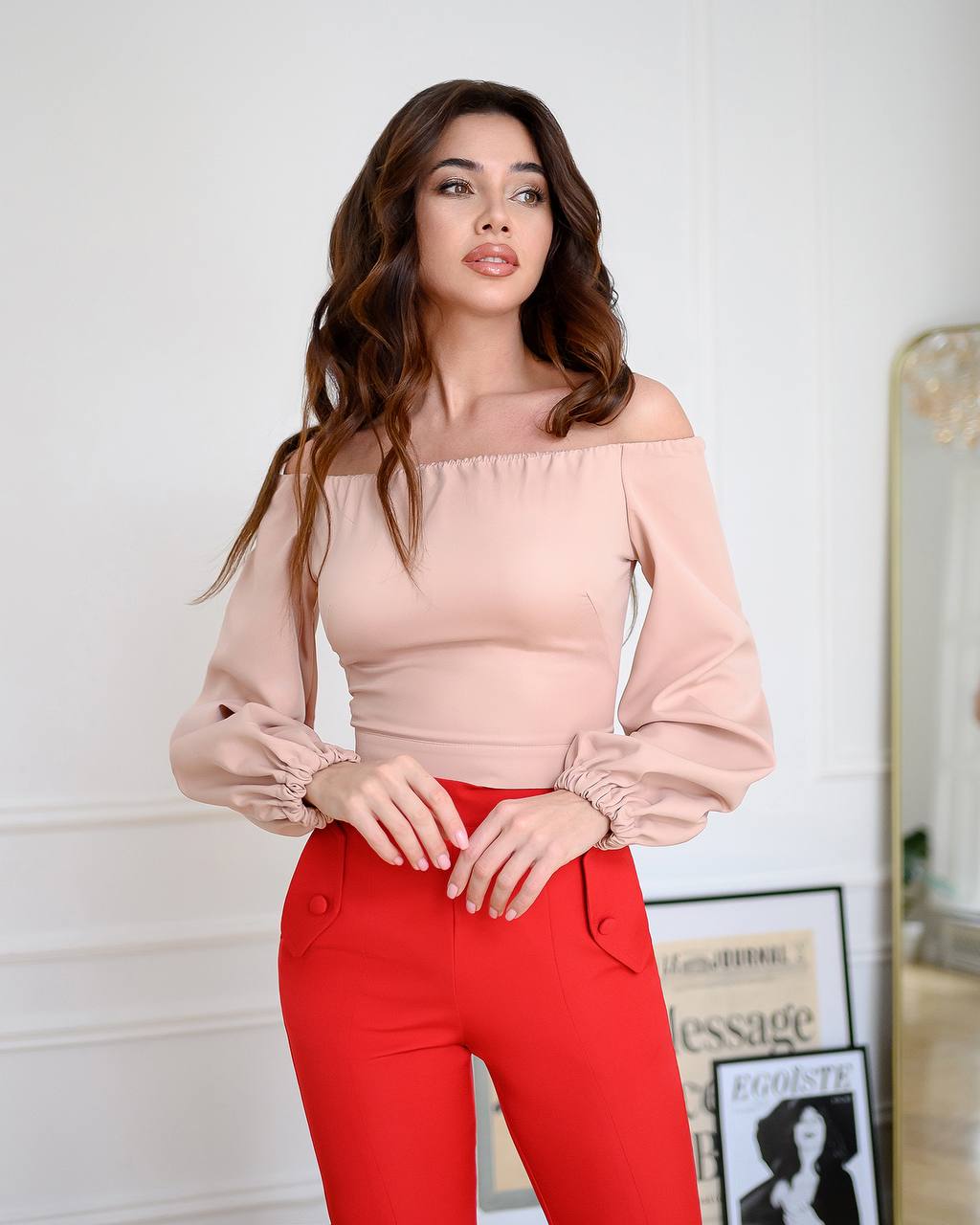Woman wearing a pink off-shoulder top and red pants in an indoor setting.
