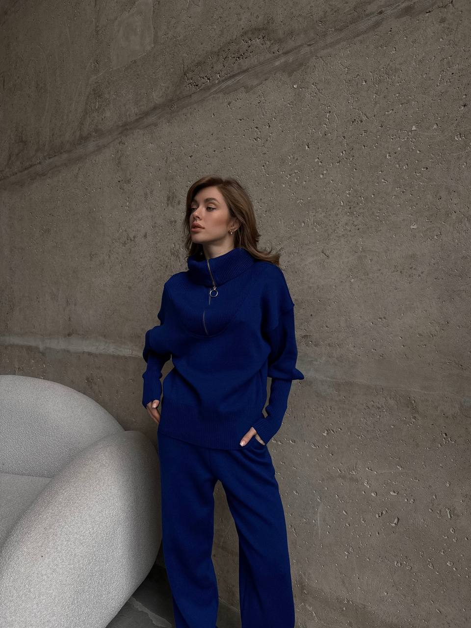 Woman in a blue outfit standing against a textured wall.