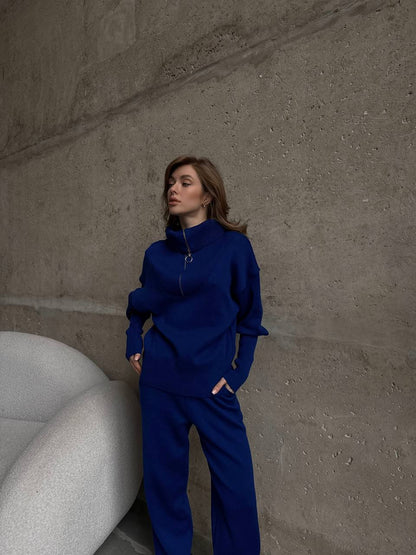Woman in a blue outfit standing against a textured wall.