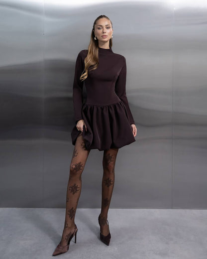 Woman wearing a brown dress and patterned stockings against a plain background