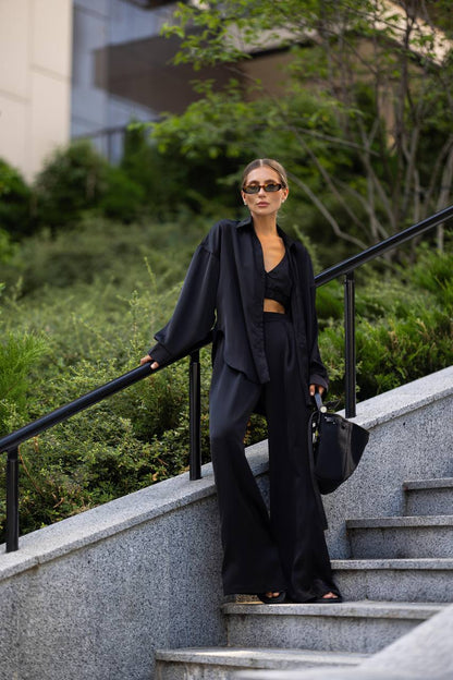 Woman in black outfit standing on outdoor steps with greenery in the background