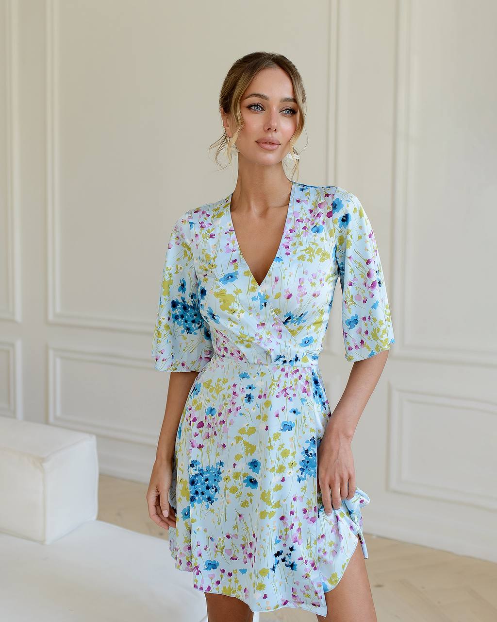 Woman wearing a floral dress in a room with white walls and furniture.
