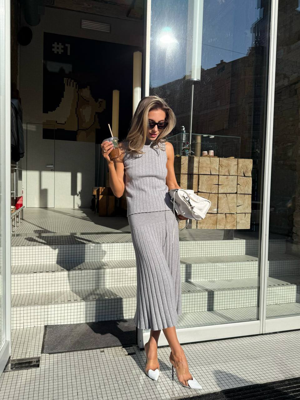 Woman in a gray outfit standing outside a building with reflective glass doors.