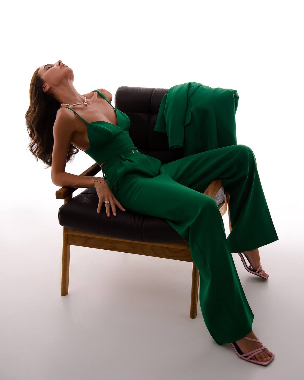Woman in a green outfit sitting on a chair against a white background