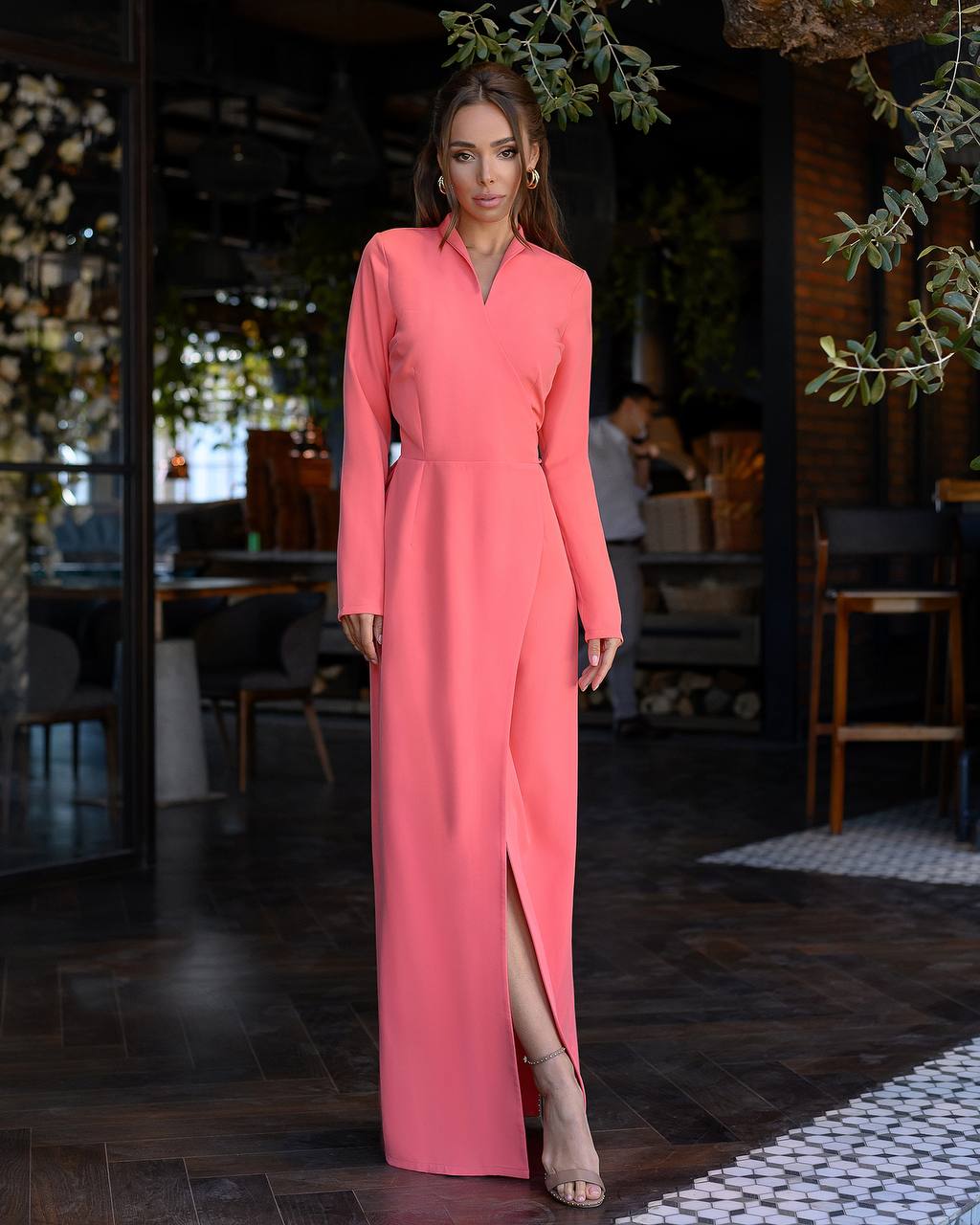 Woman wearing a long pink dress in an indoor setting with plants and furniture.