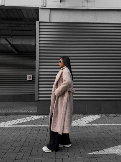 Person wearing a long coat standing on a street with a building in the background