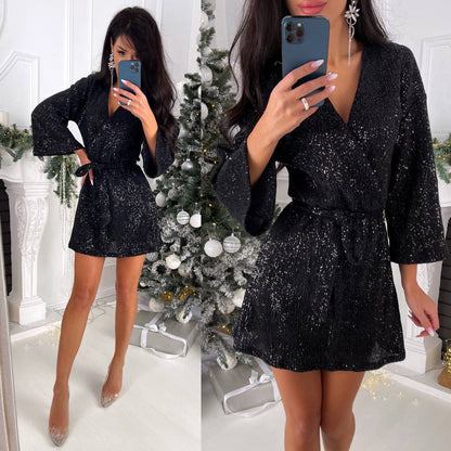 Woman in a black sequin dress taking a mirror selfie in a festive setting with a Christmas tree.