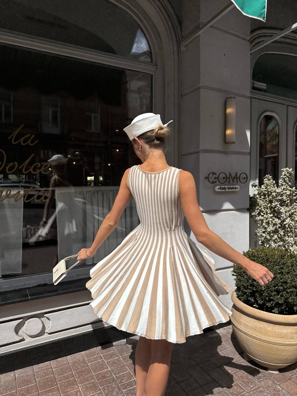 Woman in a white and beige striped dress standing in front of a store with 'GOMO' branding.