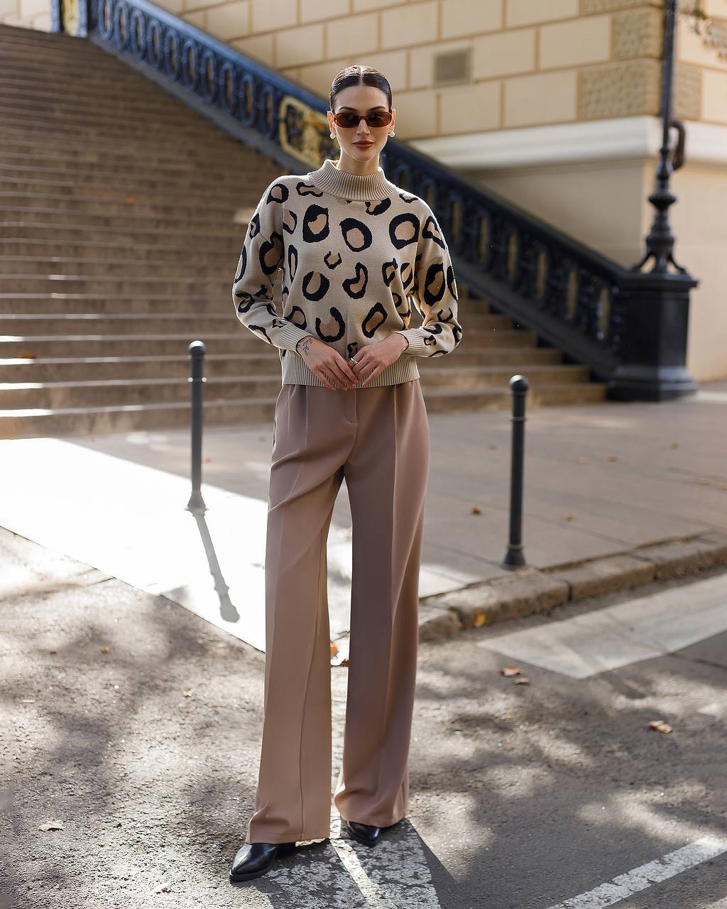 Person wearing a leopard print sweater and beige pants on a city street.