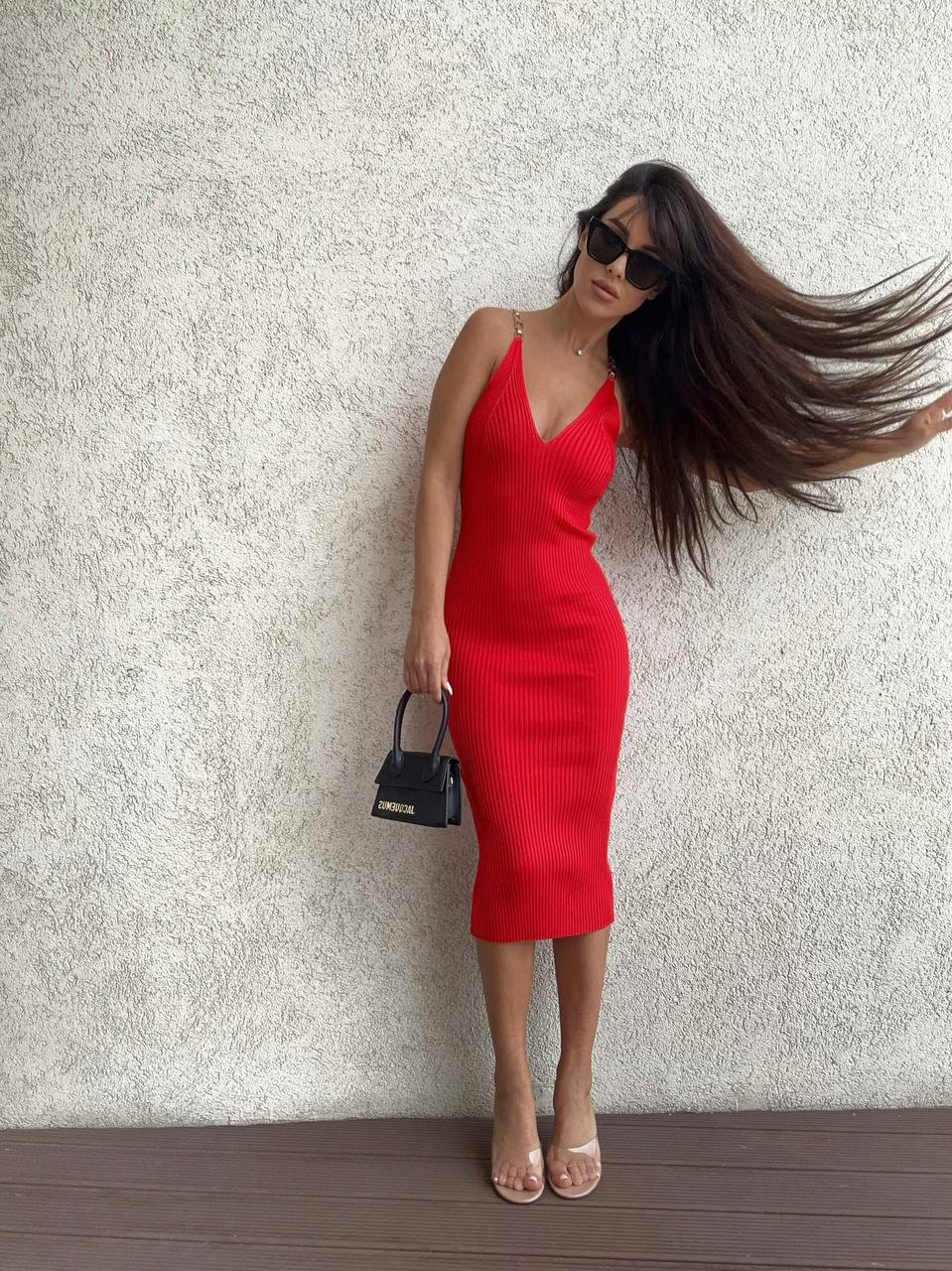 Woman in a red dress posing against a textured wall.