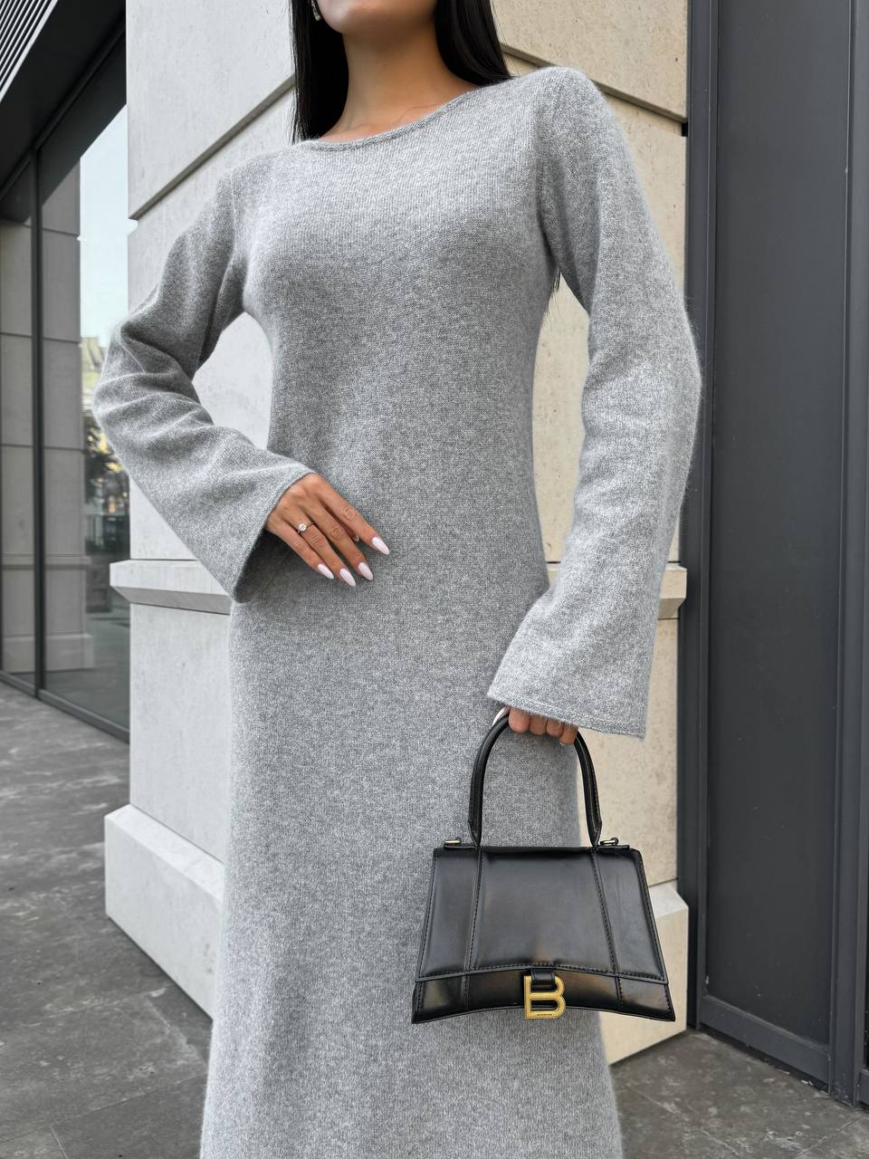 Woman wearing a gray dress holding a black handbag against a building background