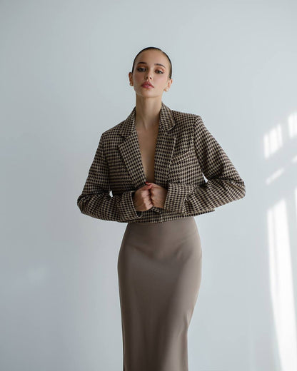 Woman wearing a houndstooth patterned jacket and beige skirt against a light background