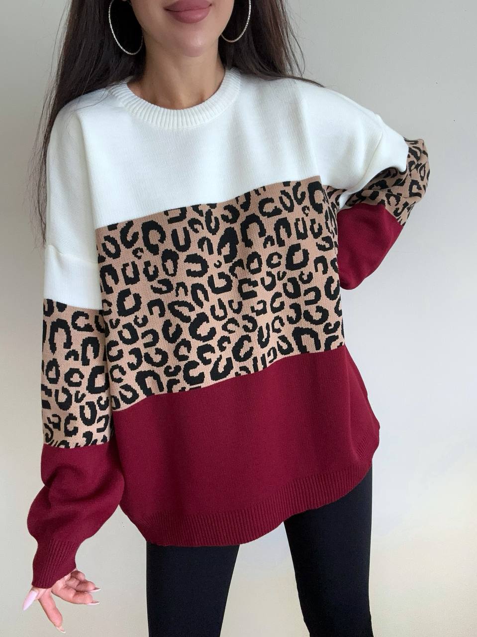 Person wearing a sweater with a leopard print pattern on a plain background