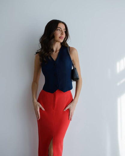 Woman wearing a navy top and red pants against a white wall