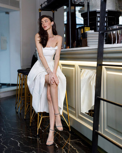 Woman in a white dress sitting at a bar counter in a stylish interior.