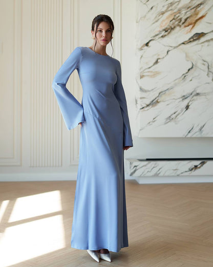 Woman wearing a light blue dress with bell sleeves in a room with marble wall.