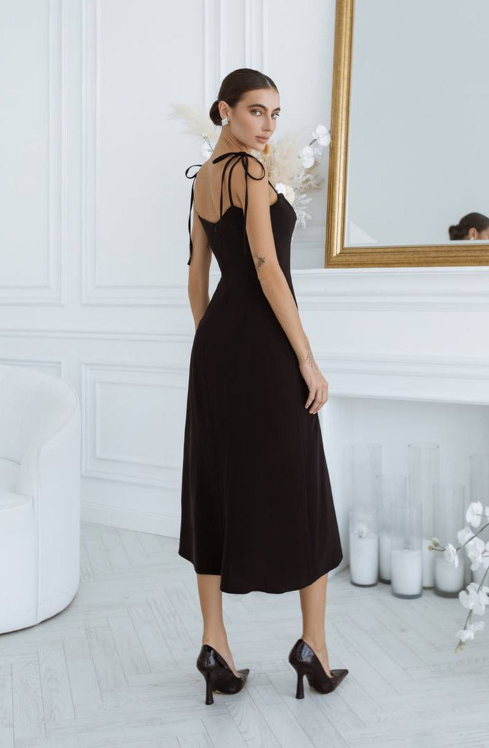 Woman in a black dress standing in a room with white walls and decorative elements.