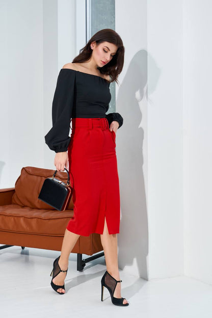 Woman in black top and red skirt standing in a minimalistic room with a brown leather couch.
