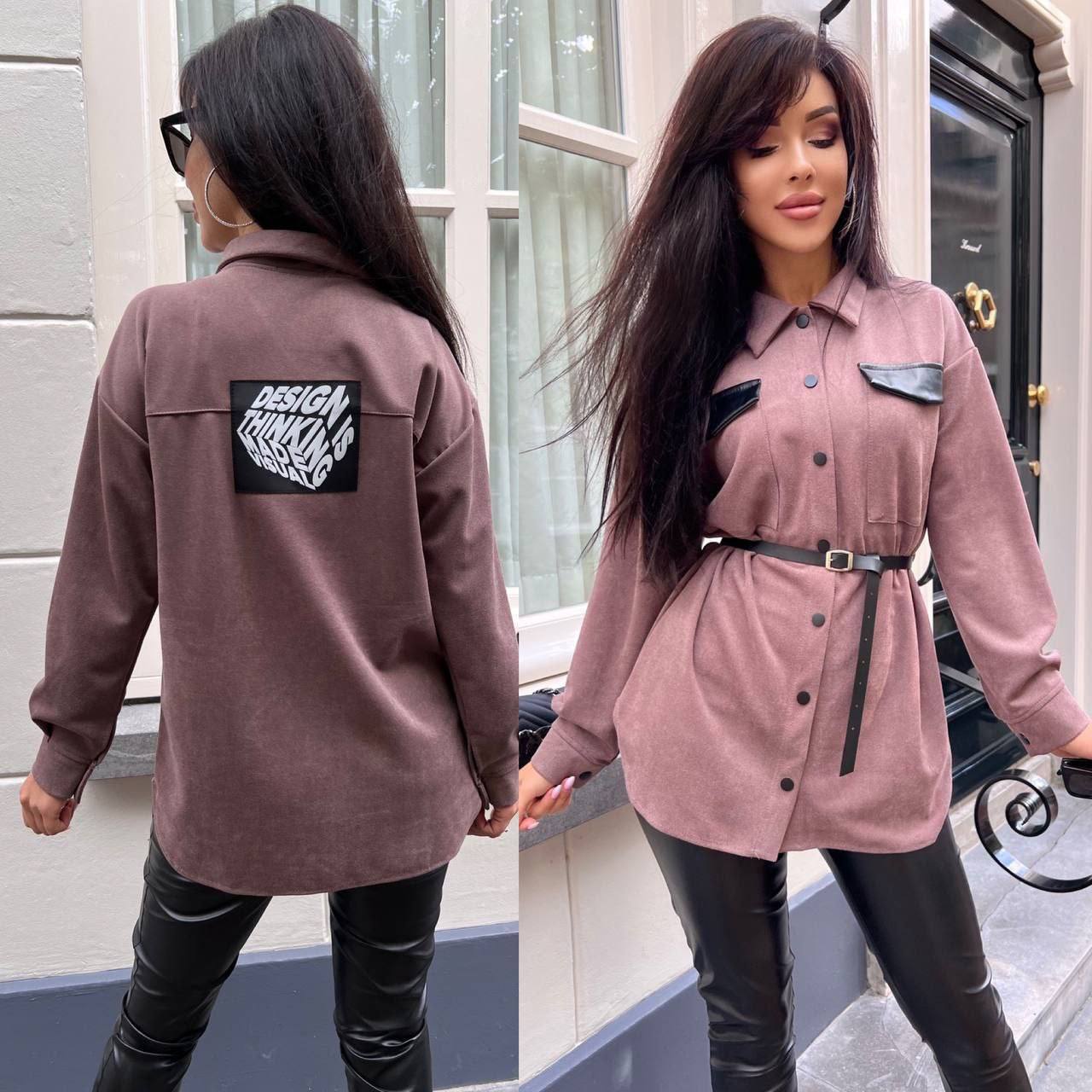 Woman wearing a pink jacket with a black patch, standing in front of a building.