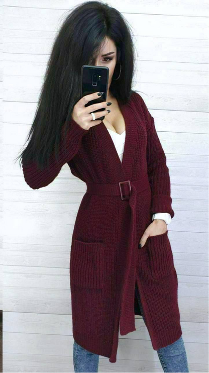 Person wearing a burgundy knitted cardigan taking a mirror selfie against a white wooden panel background.