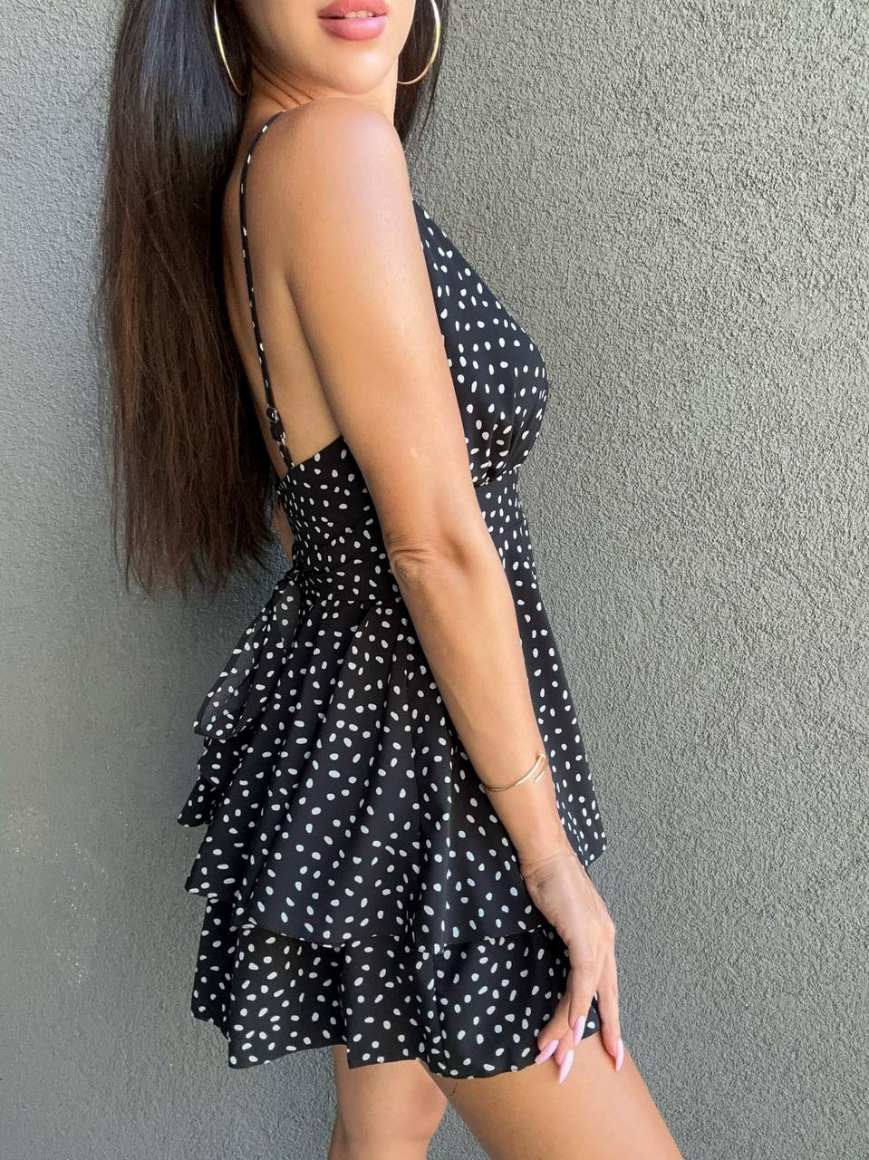Woman wearing a black polka dot dress against a gray wall
