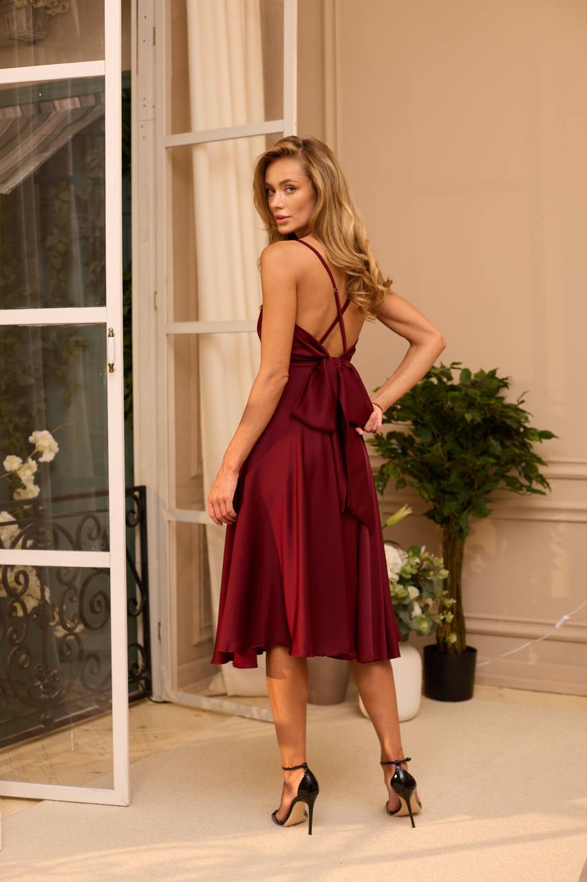 Woman in a burgundy dress standing in a stylish interior setting.