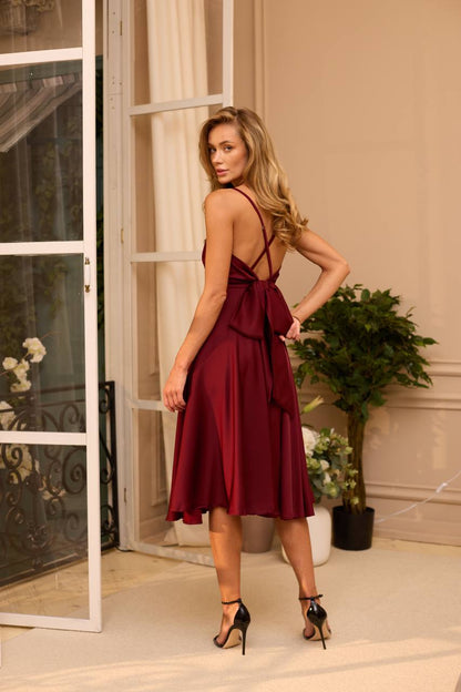 Woman in a burgundy dress standing in a stylish interior setting.