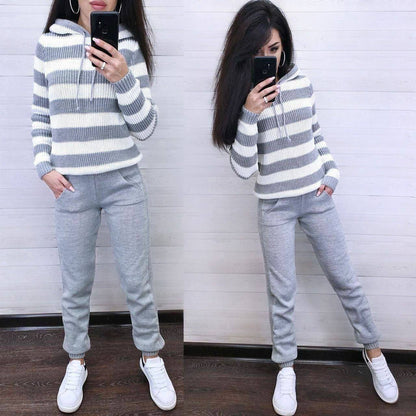 Person wearing a gray and white striped sweater and gray sweatpants, standing against a white wall.