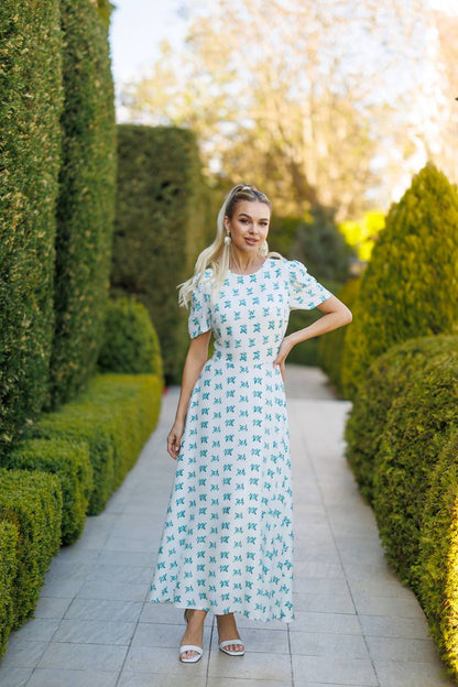 Woman in a floral dress standing in a garden with manicured hedges.
