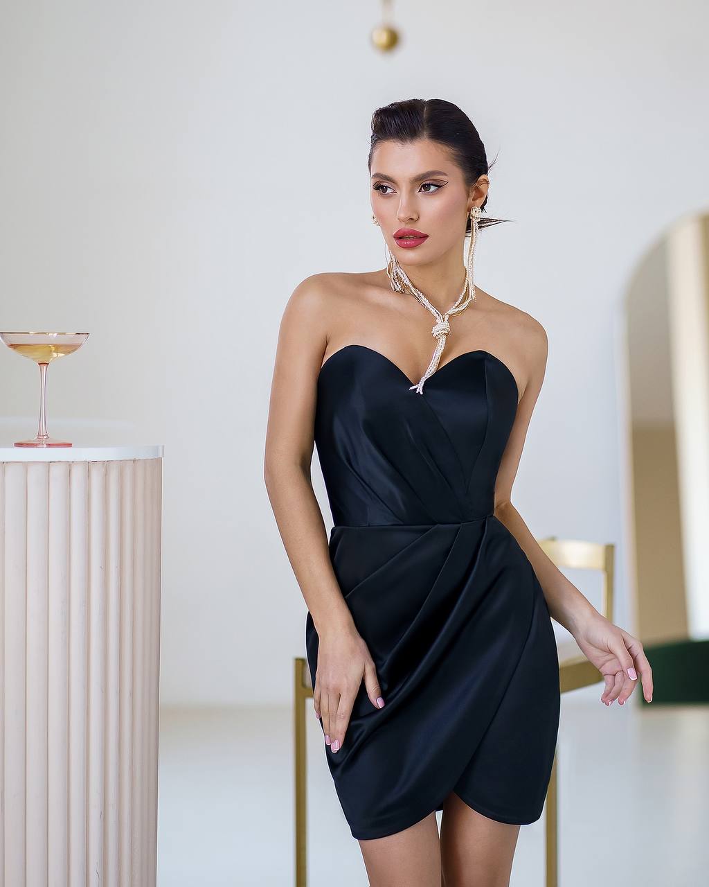 Woman in a black strapless dress standing in an elegant indoor setting.