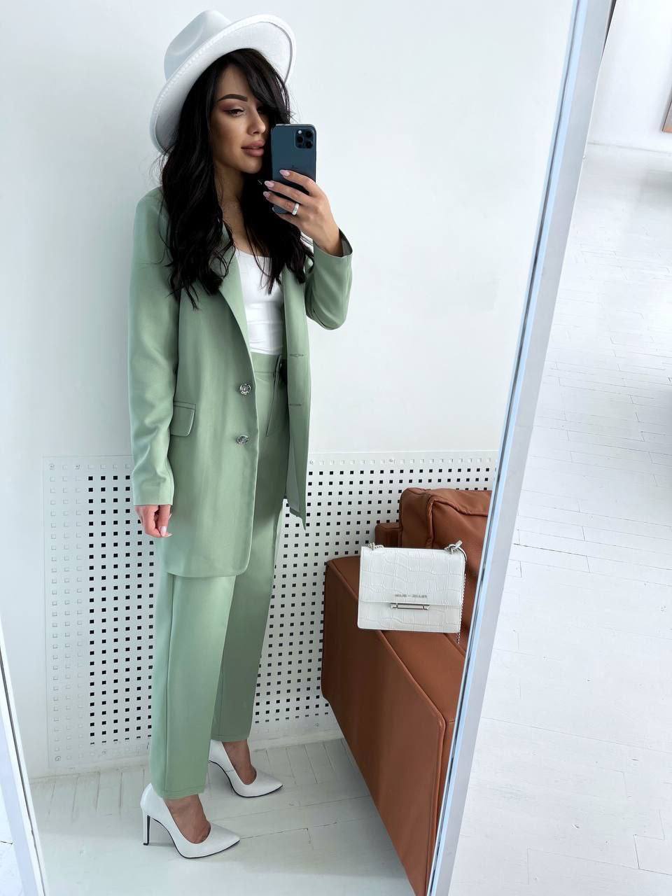 Woman taking a mirror selfie wearing a green suit and white hat.