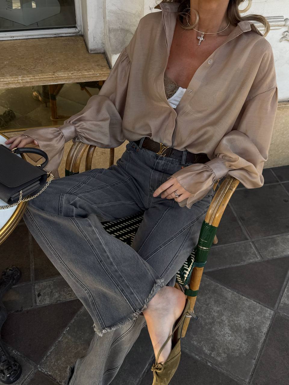 Person wearing a beige blouse and dark jeans sitting on a chair.