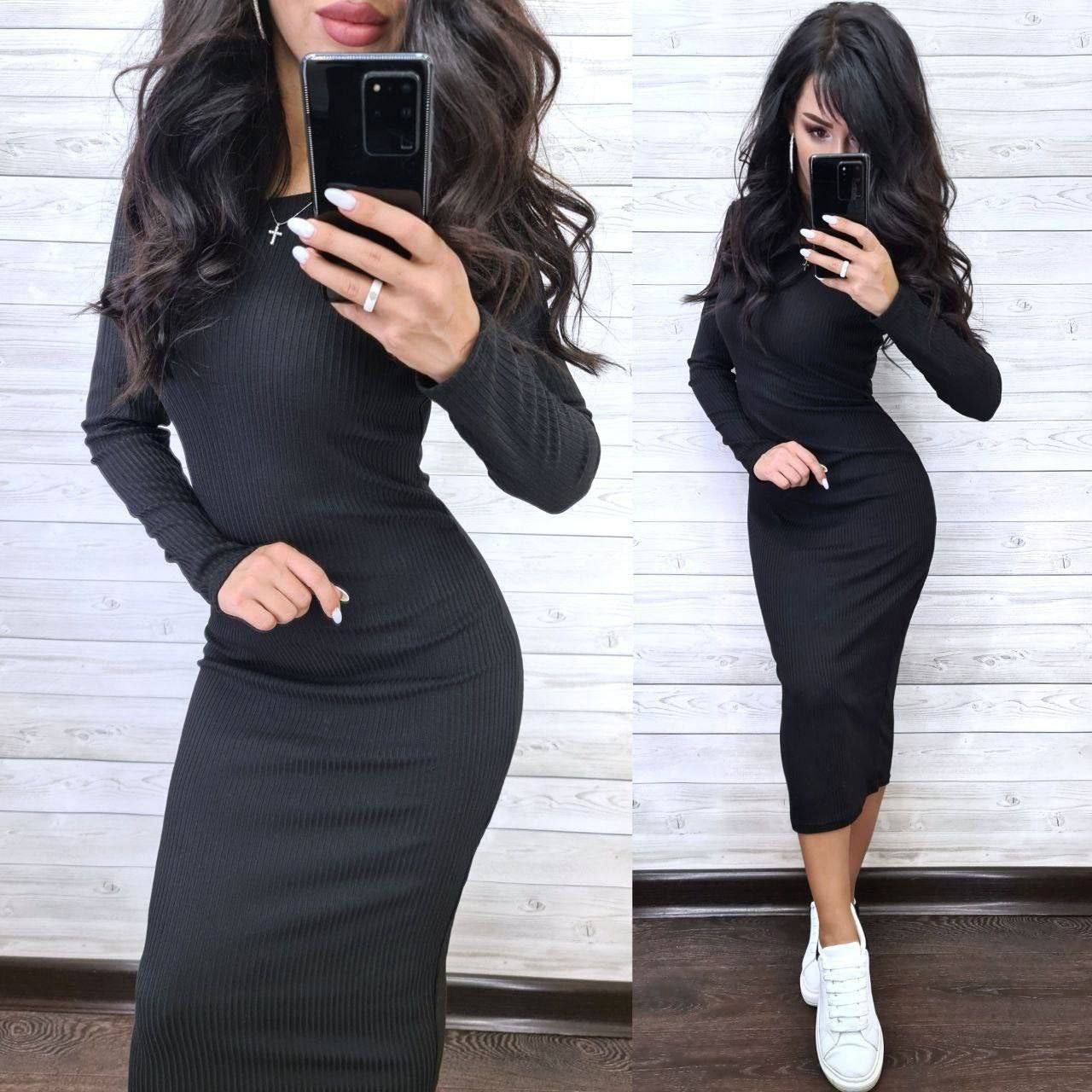 Woman wearing a black long-sleeve dress against a white wooden panel background.