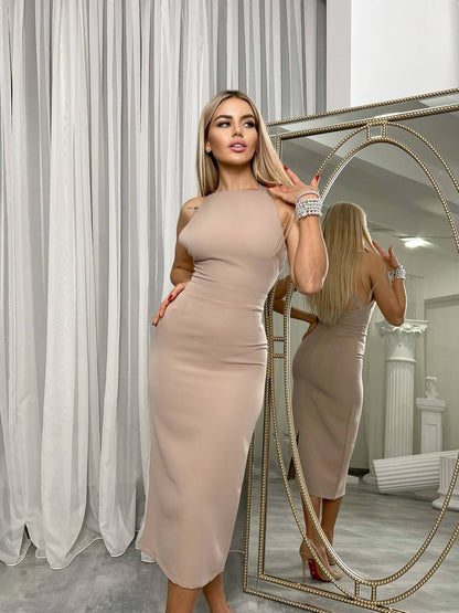 Woman in a beige dress standing in front of a mirror in a room with white curtains.