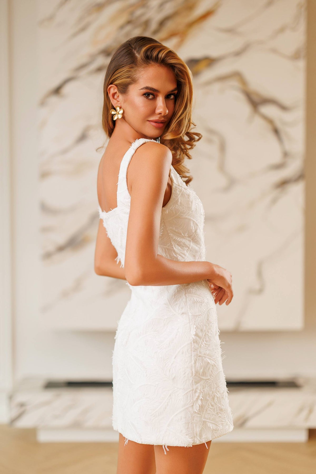 Woman in a white dress standing against a marble wall.