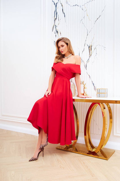 Woman in a red off-shoulder dress standing in a stylish interior setting.