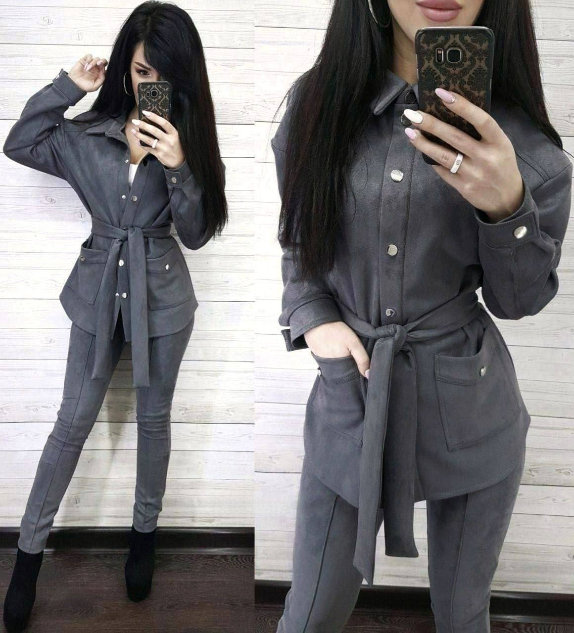 Woman wearing a gray outfit with a belt, taking a mirror selfie.