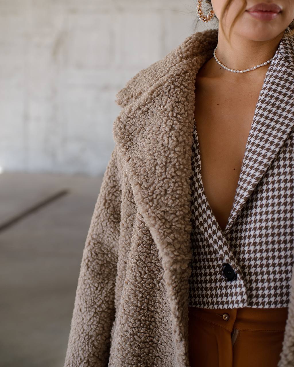 Person wearing a houndstooth patterned coat over a checkered shirt with a blurred background