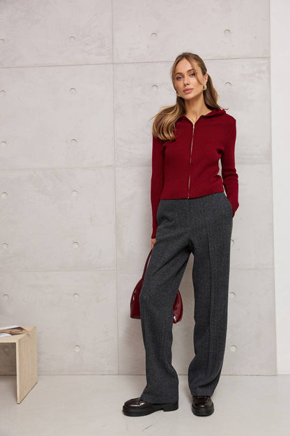 Woman wearing a red hoodie and gray pants against a light gray wall.