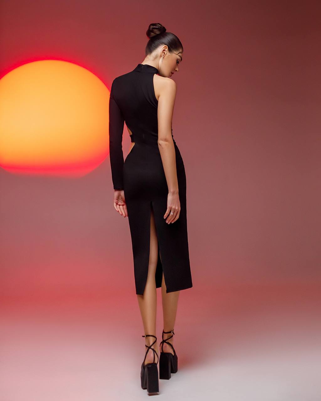Woman wearing a black dress with a high slit, standing against a gradient background with a warm light.